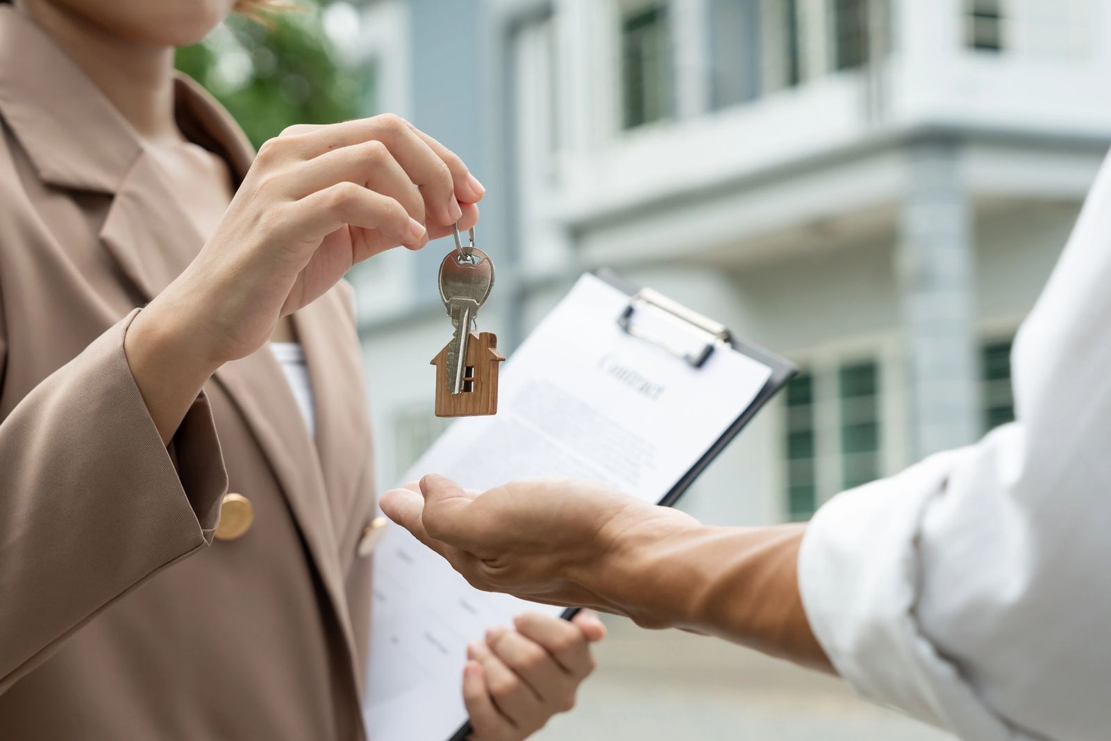 A real estate agent handing over a house key to a new owner while holding a contract on a clipboard